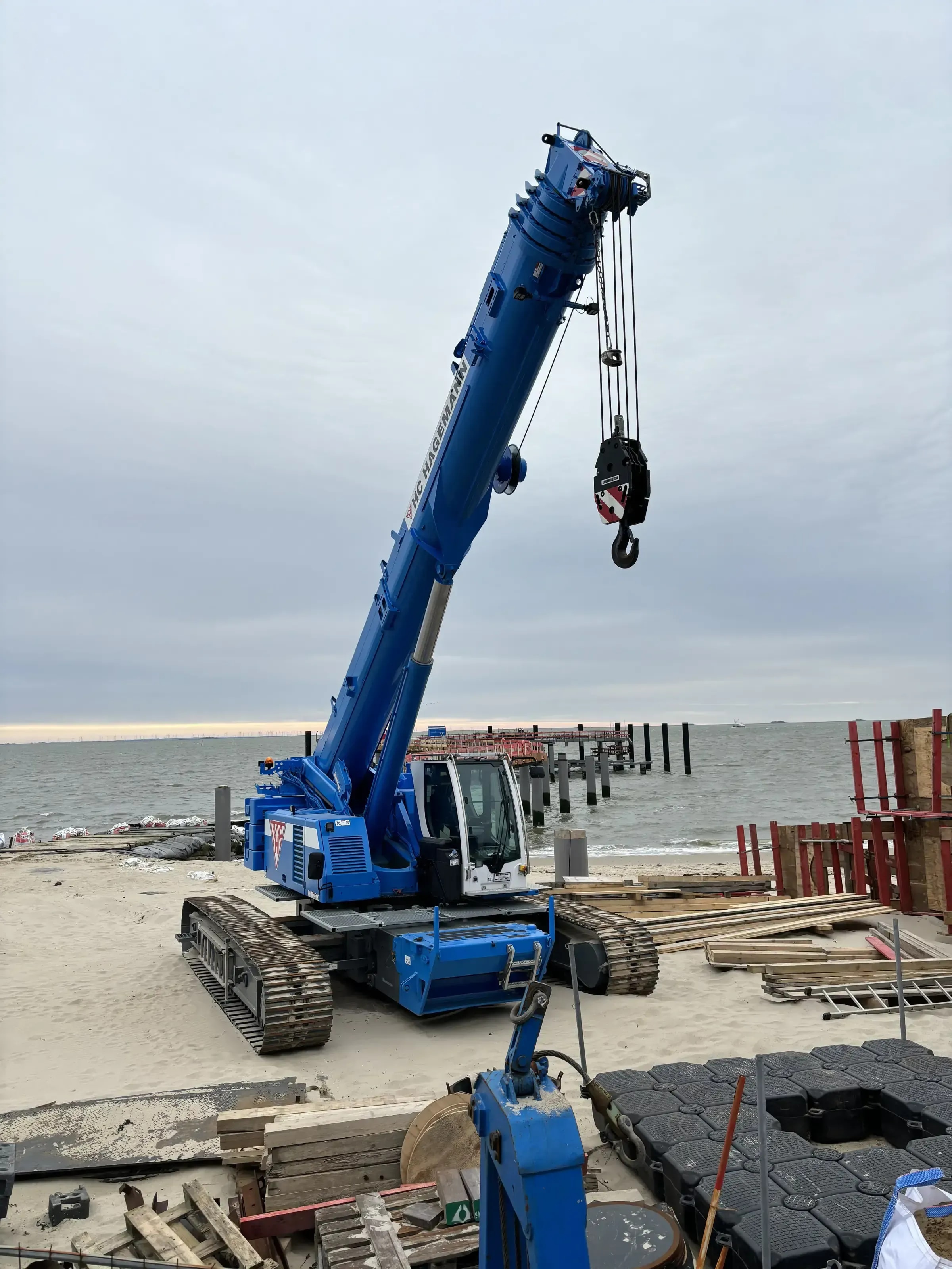 Blauer Teleskop-Raupenkran im Einsatz an Baustelle am Strand, verfuegbar zur Vermietung